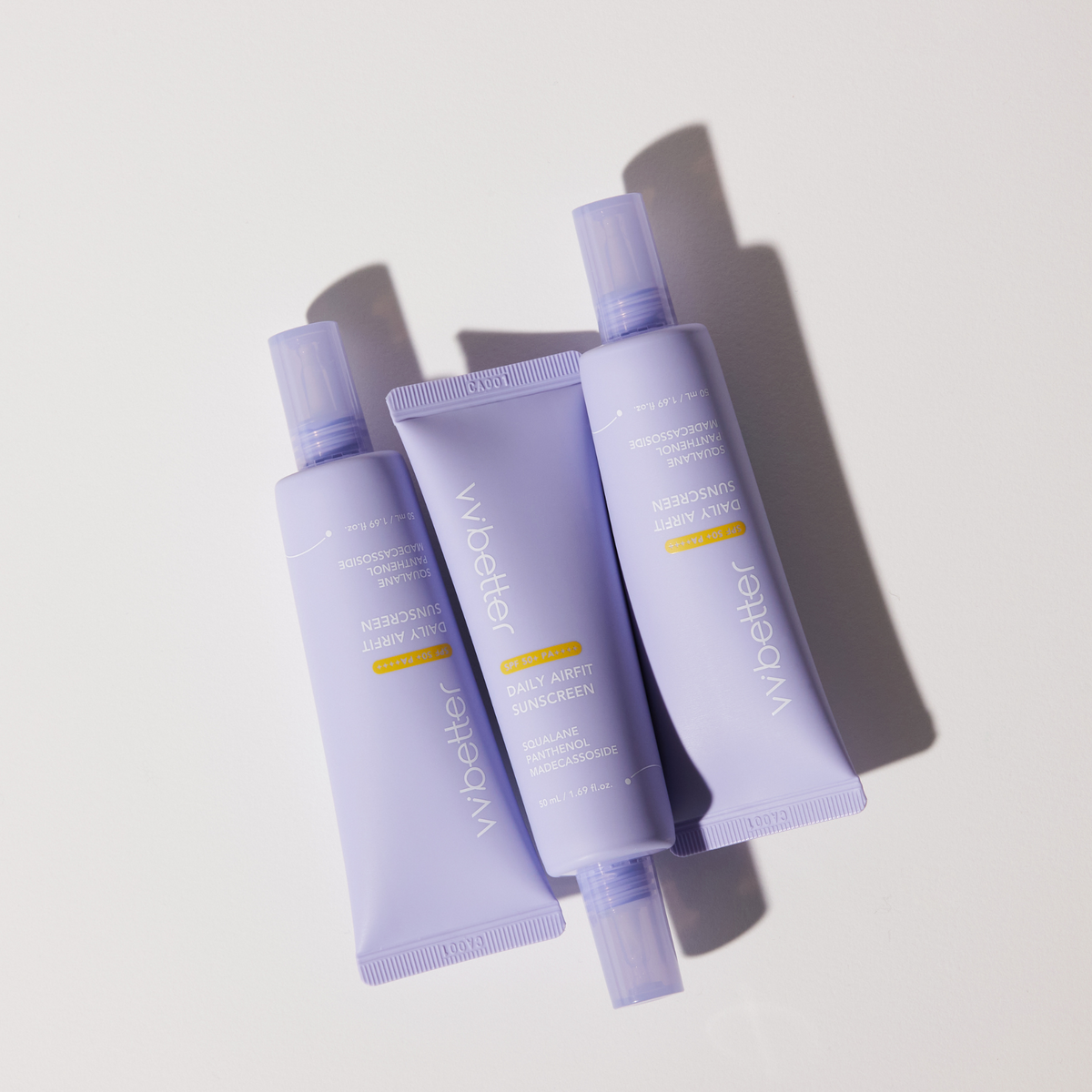 Three lavender Daily Airfit Sunscreen tubes laid out on a pale surface, overhead view