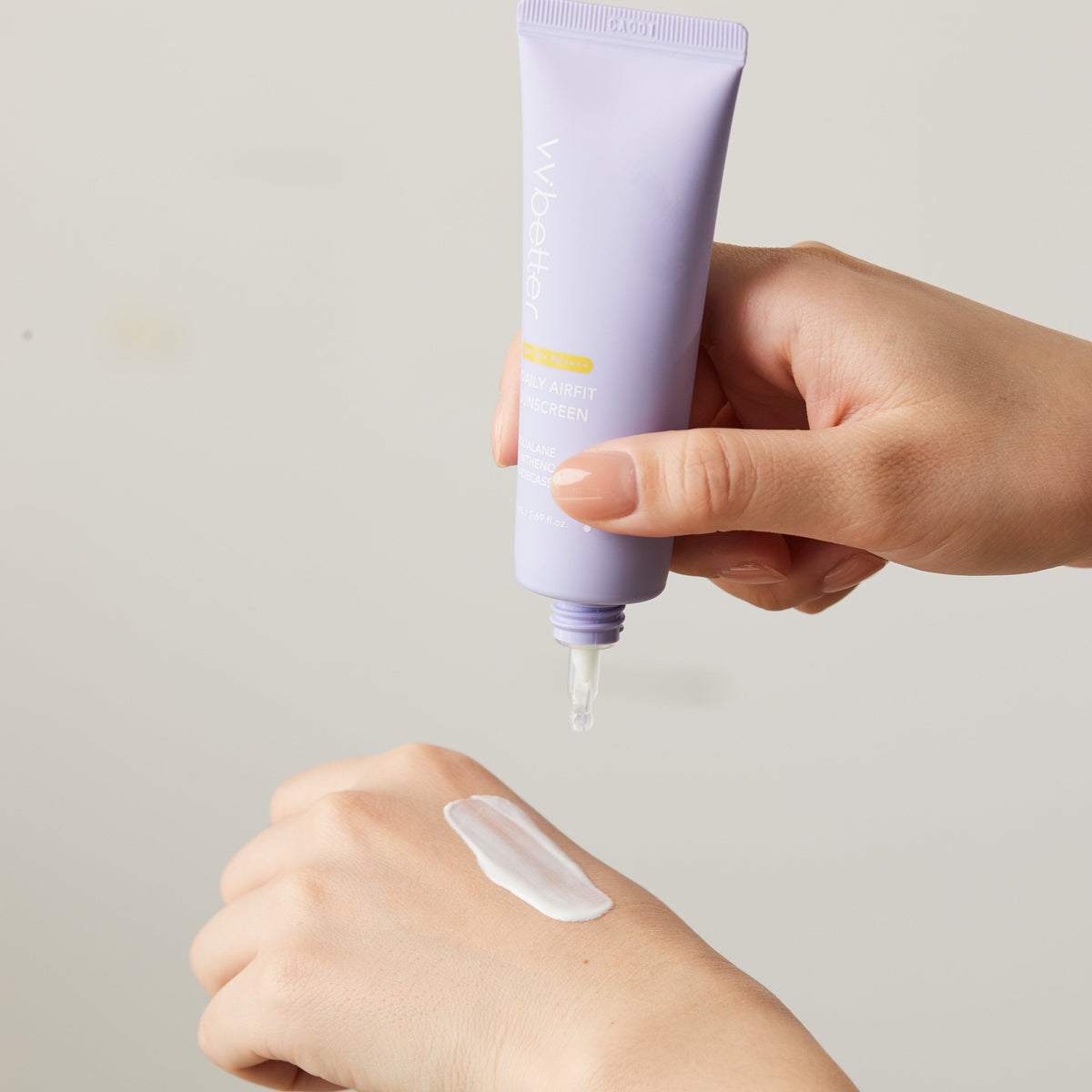 A lavender Daily Airfit Sunscreen tube being squeezed to place a line of cream on the back of a hand