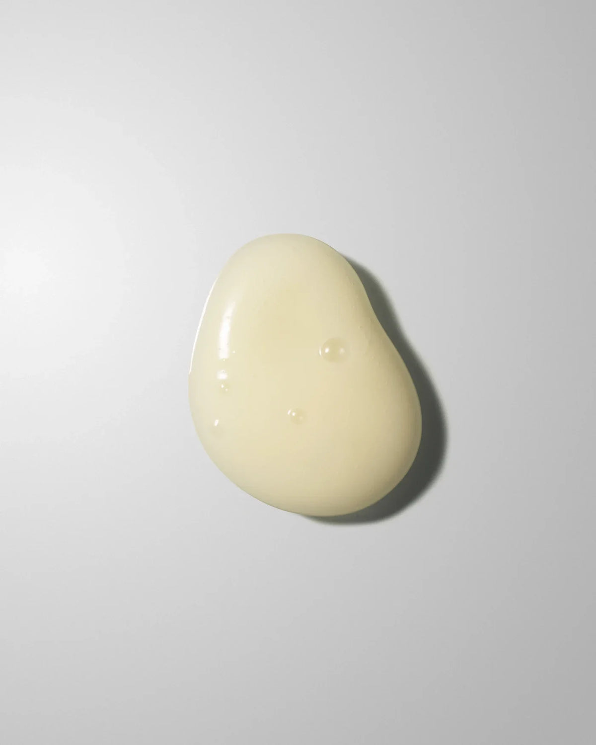 A cream-coloured swatch of serum on a pale grey surface, from the Dark Spot Solution Vita C TRX Serum editorial photograph