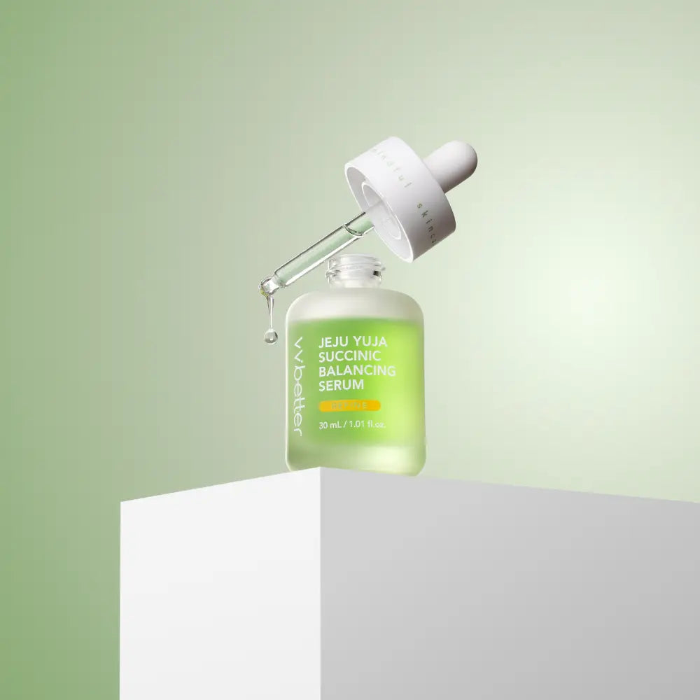 Jeju Yuja Succinic Balancing Serum — bottle on a white pedestal with the dropper lifted, soft green backdrop