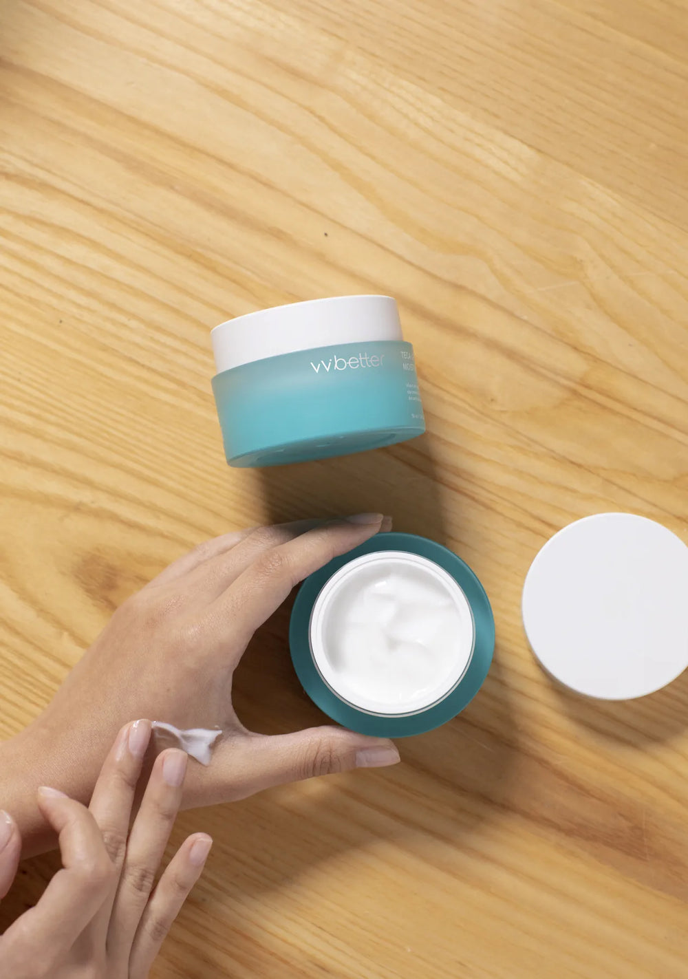 Teca Lifting Moisture Cream jar open on a wooden table while a hand takes a little cream