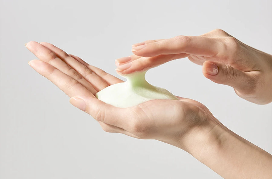 Two hands lifting soft pale-green foam between the fingertips