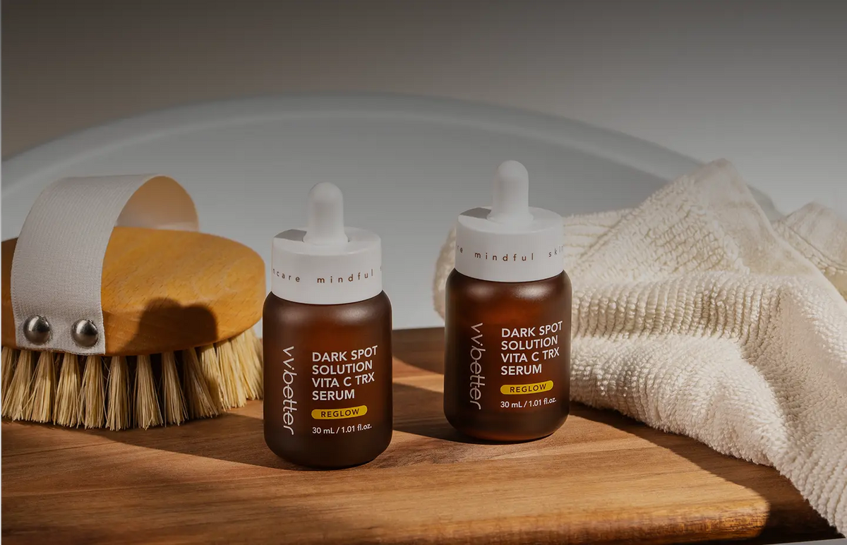 Two dark brown Dark Spot Solution Vita C TRX Serum dropper bottles on a wooden tray beside a brush and a cloth