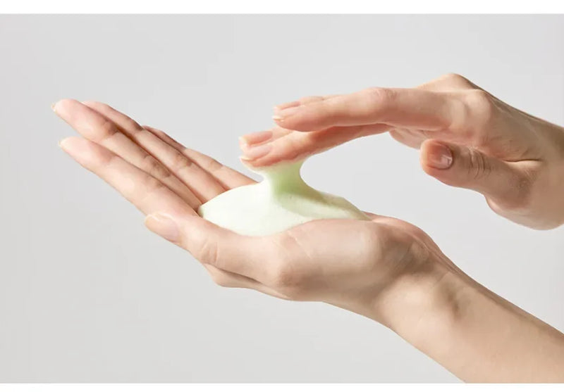Hands working light-green cleanser foam in the palms before applying it to the face