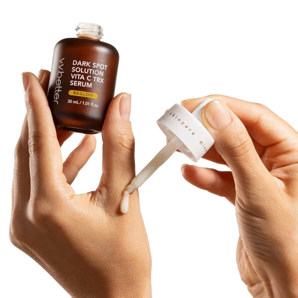 Hands holding a Dark Spot Solution Vita C TRX Serum bottle while a dropper is lifted from it