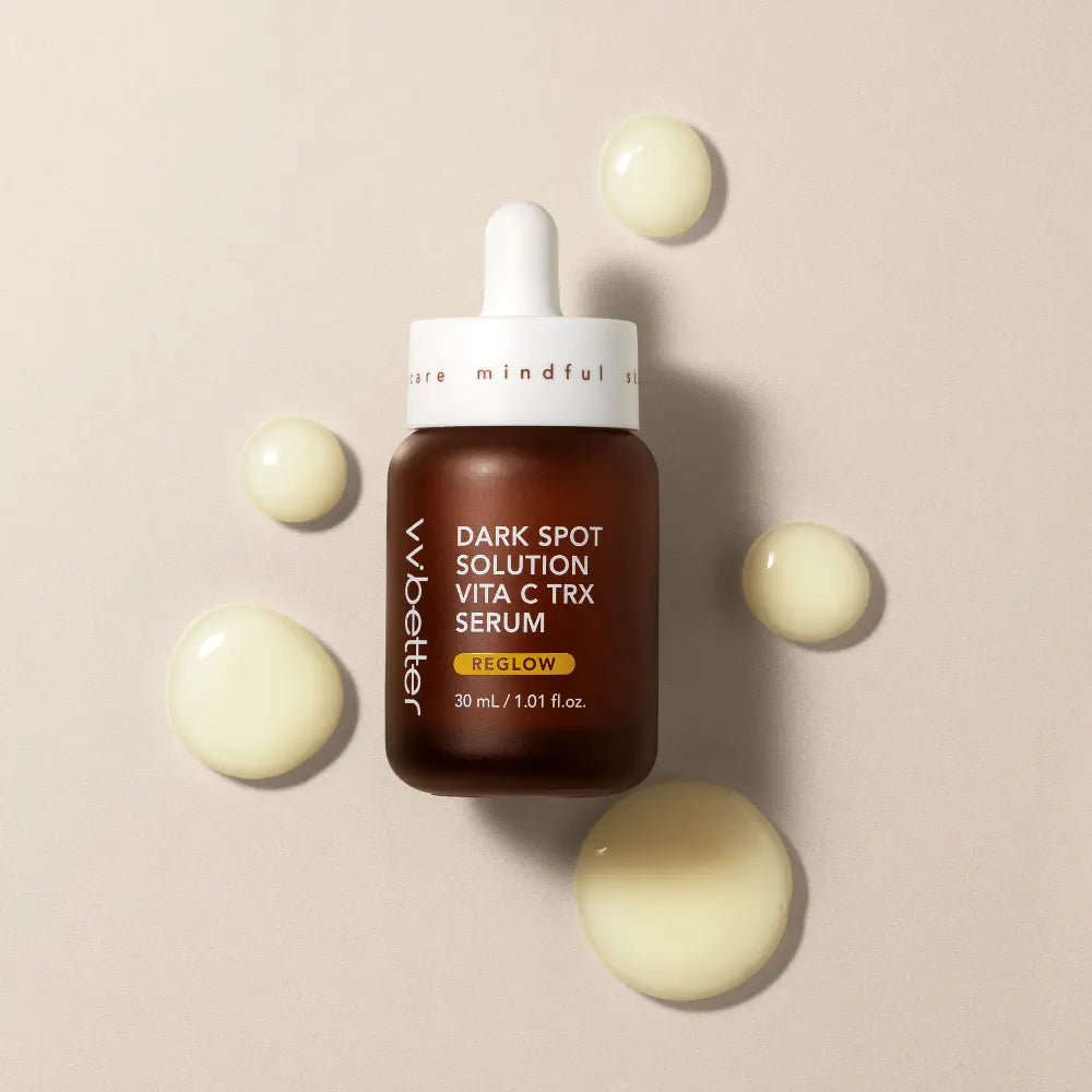 Dark Spot Solution Vita C TRX Serum — bottle lying flat beside pale yellow serum droplets, overhead view