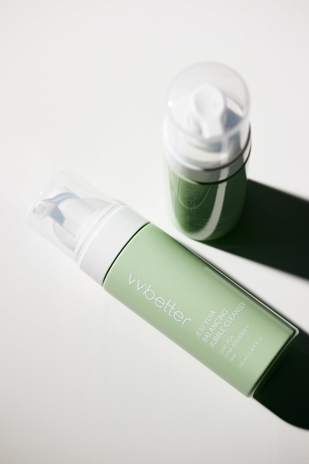 Jeju Yuja Balancing Bubble Cleanser — bottle lying down with the clear pump cap beside it, angle view