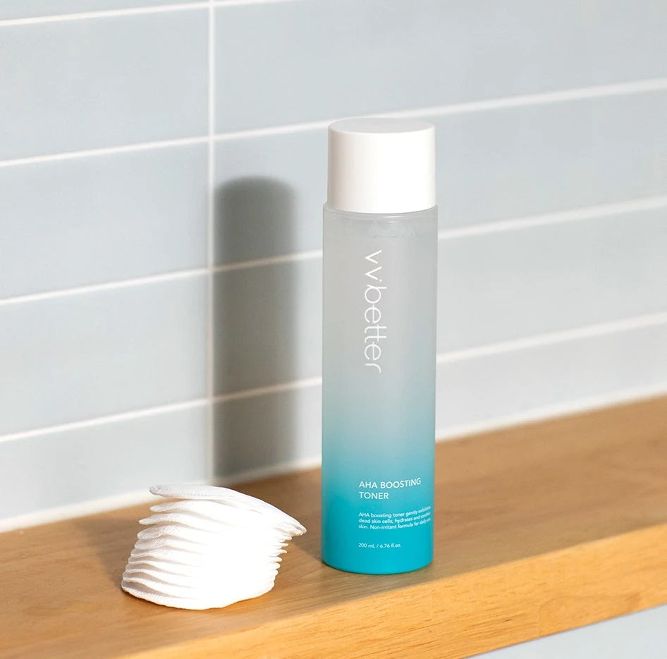 VVBETTER AHA Boosting Toner bottle on a wooden shelf beside a stack of cotton pads