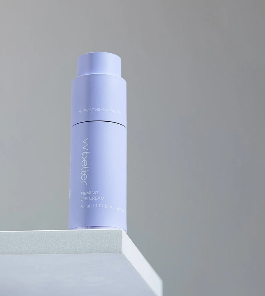 Firming Eye Cream bottle on a white block against a dark grey wall