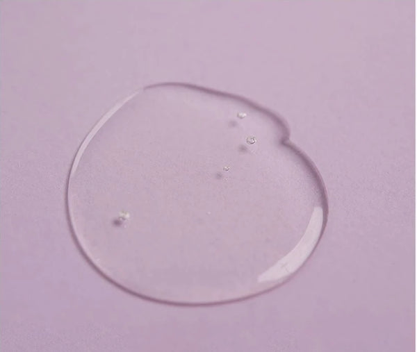 Clear drop of cleansing oil on lilac paper