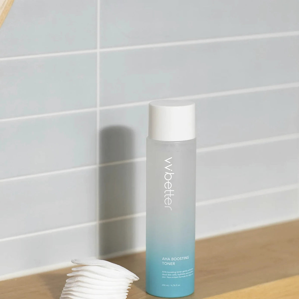 AHA Boosting Toner, made with betaine salicylate, beside a stack of cotton pads on a wooden shelf