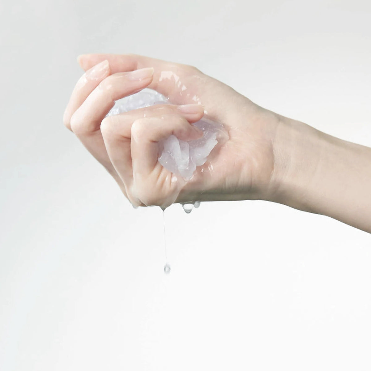 A hand squeezing the Rejuvenating Squalane Mask sheet, made with three types of hyaluronic acid, so drops of essence fall