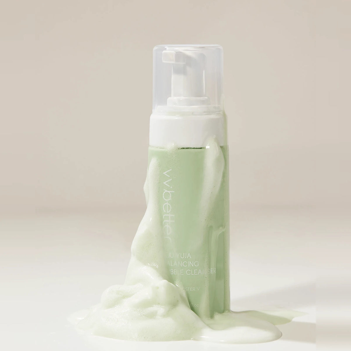 Soft green foam of the Jeju Yuja Balancing Bubble Cleanser, made with 0.5% salicylic acid, flowing down the bottle on a cream background