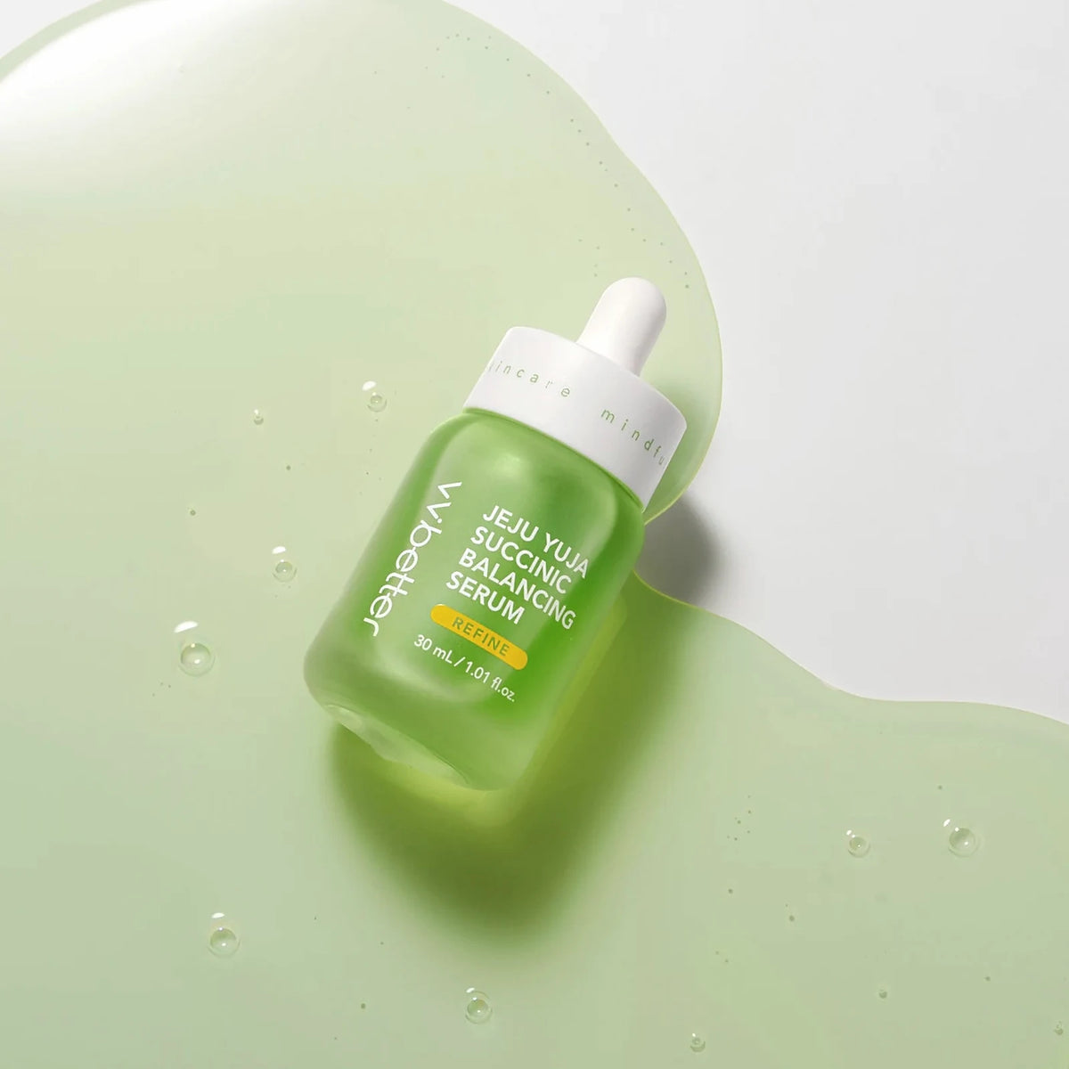The Jeju Yuja Succinic Balancing Serum bottle lying in a pool of its clear green serum