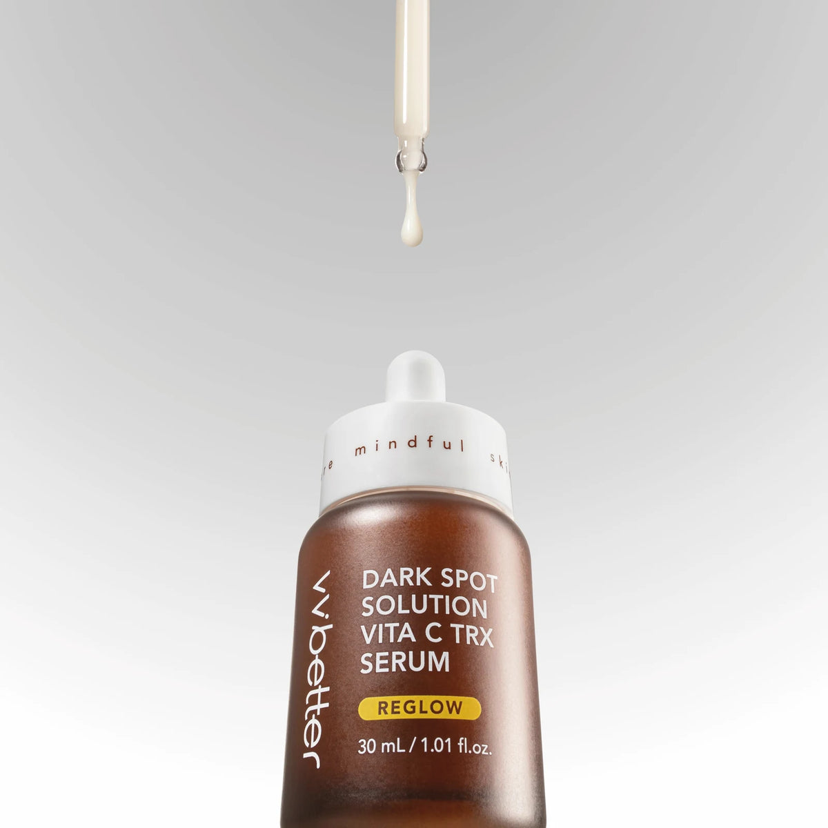 A single drop of Dark Spot Solution Vita C TRX Serum falling from the glass dropper into the amber REGLOW bottle on a soft grey background