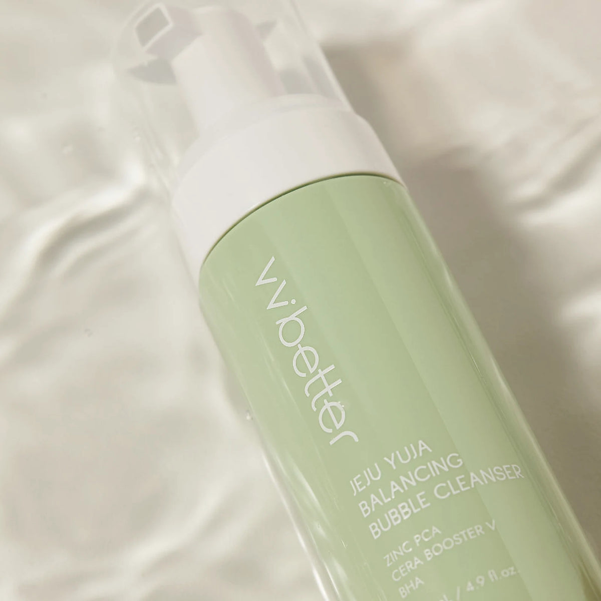 The pale green Jeju Yuja Balancing Bubble Cleanser bottle, its label naming zinc PCA, resting in clear rippling water